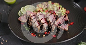 Teriyaki or soy sauce pours on sliced grilled fried tuna steak covered with sesame seeds and traditional salsa garnish