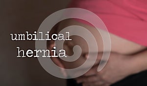 Term UMBILICAL HERNIA.Young pregnant woman touches her belly in the background