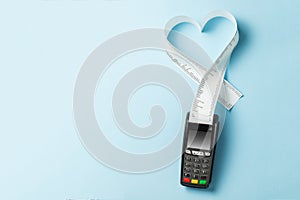Terminal cash register machine POS for payments and long roll paper cash tape in heart shaped on blue background. Copy space for