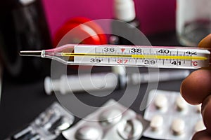 A termometr with high temperature in hand and different medicines photo