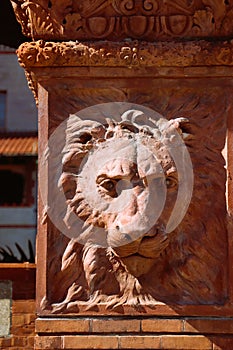 Terra cotta lion face medallion in red brick column in sun