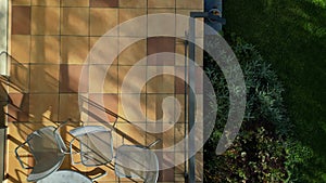 terrace by house.paving tiles brown and yellow. oval table, chair metal railing