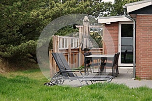 a Terrace with table and chairs and 2 summer loungers and a parasol and a small green garden surrounded by hedges