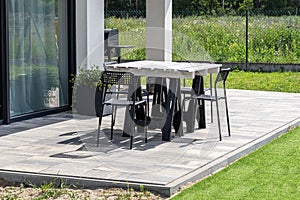 Terrace table made of white pallet standing on plastic trestles, black plastic chairs.