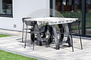 Terrace table made of white pallet standing on plastic trestles, black plastic chairs.