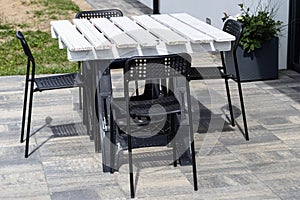 Terrace table made of white pallet standing on plastic trestles, black plastic chairs.