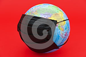 Terrestrial globe model with black surgical mask isolated on red background. Concept: Quarantined earth.