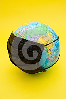 Terrestrial globe model with black surgical mask isolated on yellow background