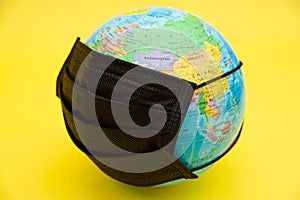 Terrestrial globe model with black surgical mask isolated on yellow background. Concept: Planet Earth in protection against