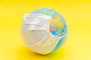 Terrestrial globe model with white surgical mask isolated on yellow background