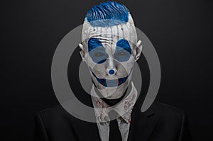 Terrible clown and Halloween theme: Crazy blue clown in black suit isolated on a dark background in the studio