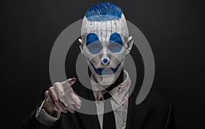 Terrible clown and Halloween theme: Crazy blue clown in black suit isolated on a dark background in the studio