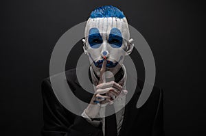 Terrible clown and Halloween theme: Crazy blue clown in black suit isolated on a dark background in the studio