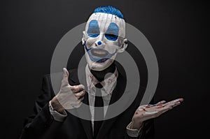 Terrible clown and Halloween theme: Crazy blue clown in black suit isolated on a dark background in the studio