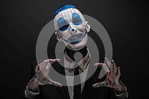 Terrible clown and Halloween theme: Crazy blue clown in black suit isolated on a dark background in the studio