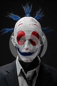 Terrible clown and Halloween theme: Crazy terrible blue clown in black suit isolated on a dark background in the studio