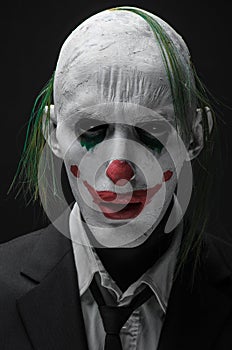 Terrible clown and Halloween theme: Crazy terrible green clown in black suit isolated on a dark background in the studio