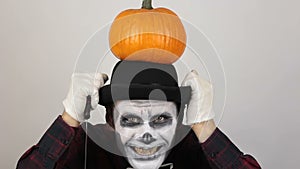 A terrible man in clown makeup and with a pumpkin on his head grimaces and waves his hand in greeting to his victim. A