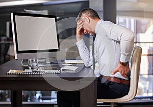That terrible pain is back. a businessman experiencing back pain while sitting at his desk.