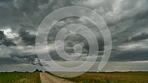 A terrible rain cloud hangs over an agricultural field and a dirt road. Hurricane and thunder over a green meadow. Climate change