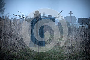 Terrible scarecrow in dark cloak and dirty hat stands alone on a cemetery