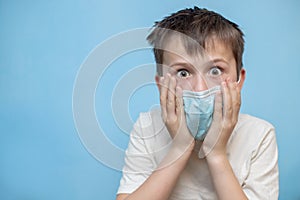 terrified boy in medical protective mask grabbed face with hands. hild with flu, influenza or cold protected from viruses, in bad