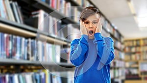 Terrified boy over book shelves at library