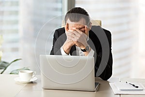 Terrified businessman covering face with hands in front of lapto