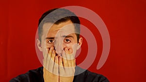 A terrified man clutches his face against a red background