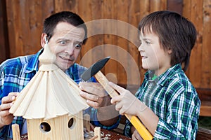 Terrified man holding nail while son handles the hammer