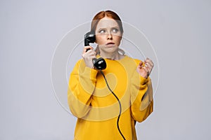 Terrified scared young woman wearing stylish yellow sweater talking on retro phone looking away.