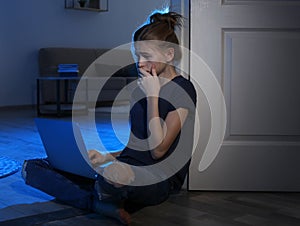 Terrified teenage girl with laptop on floor in dark room