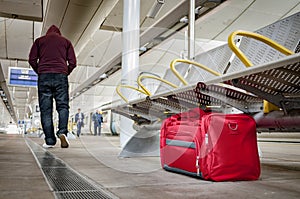 Terrorism and public safety concept with an unattended bag left under chair on platform at train station or airport and man