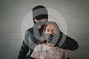 Terrorist and scared little hostage girl with Closed mouth on dark background. concept of kidnapping.