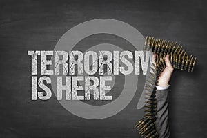 Terrorist text on blackboard with businessman hand holding ammunition
