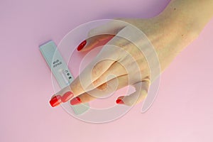 test for coronavirus lies on a pink background. a girl with a red manicure applies a punctured finger to take blood. sensitive