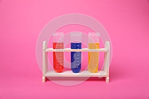 Test tubes with colorful liquids in wooden stand on bright pink background. Kids chemical experiment set