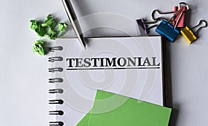 TESTIMONIAL - words in a notebook with stationery clips, pen and green papers