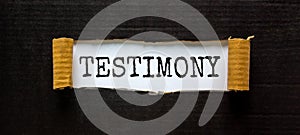 Testimony symbol. The word `Testimony` appearing behind torn black paper. Beautiful black background. Business, testimony concep