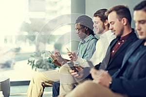 Testing their social networking skills. a group of businessmen using different wireless devices while waiting in line