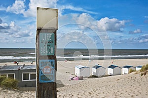 Wooden post at beach with retro style signs saying `Life is good at the beach` and `Tropical Bar` with ocean in background