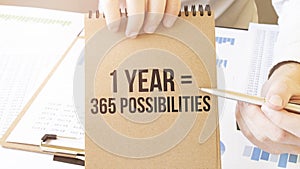 Text 1 Year 365 Possibilities on brown paper notepad in businessman hands on the table with diagram. Business concept