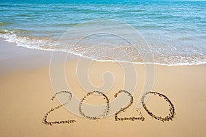 Text 2020 Happy New Year on the beach with waves and clear blue sea. 2020 numbers on the coast. Hand written messages in sand on a