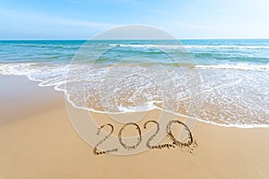 Text 2020 Happy New Year on the beach with waves and clear blue sea. 2020 numbers on the coast. Hand written messages in sand on a