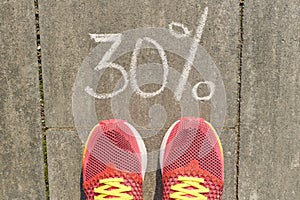 Text 30 percent written on gray pavement with woman legs in sneakers, view from above