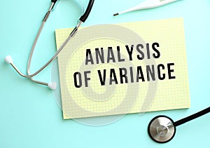 The text ANALYSIS OF VARIANCE is written in a yellow pad that lies next to the stethoscope on a blue background
