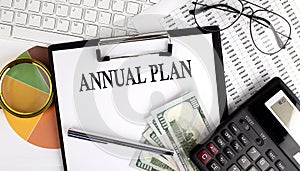 Text ANNUAL PLAN on Office desk table with keyboard,dollars,calculator ,supplies,analysis chart on white background