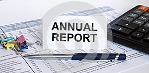 Text Annual Report on white card with blue metal pen, calculator and paper clips on financial table