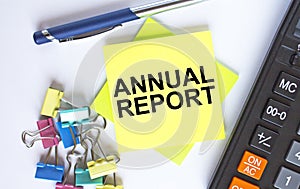 Text Annual Report on yellow stickers with calculator, blue pen and paper clips