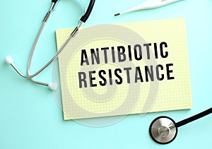 The text ANTIBIOTIC RESISTANCE is written in a yellow pad that lies next to the stethoscope on a blue background.